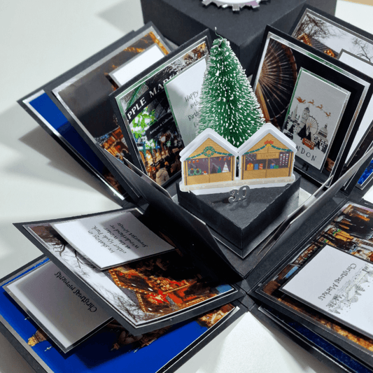 A close-up of a Christmas card featuring a festive design, placed in a box alongside a miniature Christmas tree, evoking a cozy holiday atmosphere.