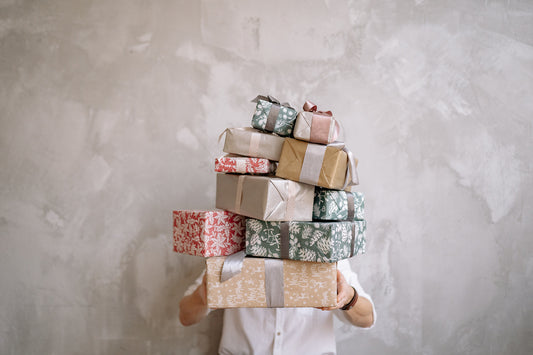 A person indoors holding a stack of wrapped presents featuring red and white gift wrap, showcasing a close-up view of festive packaging.