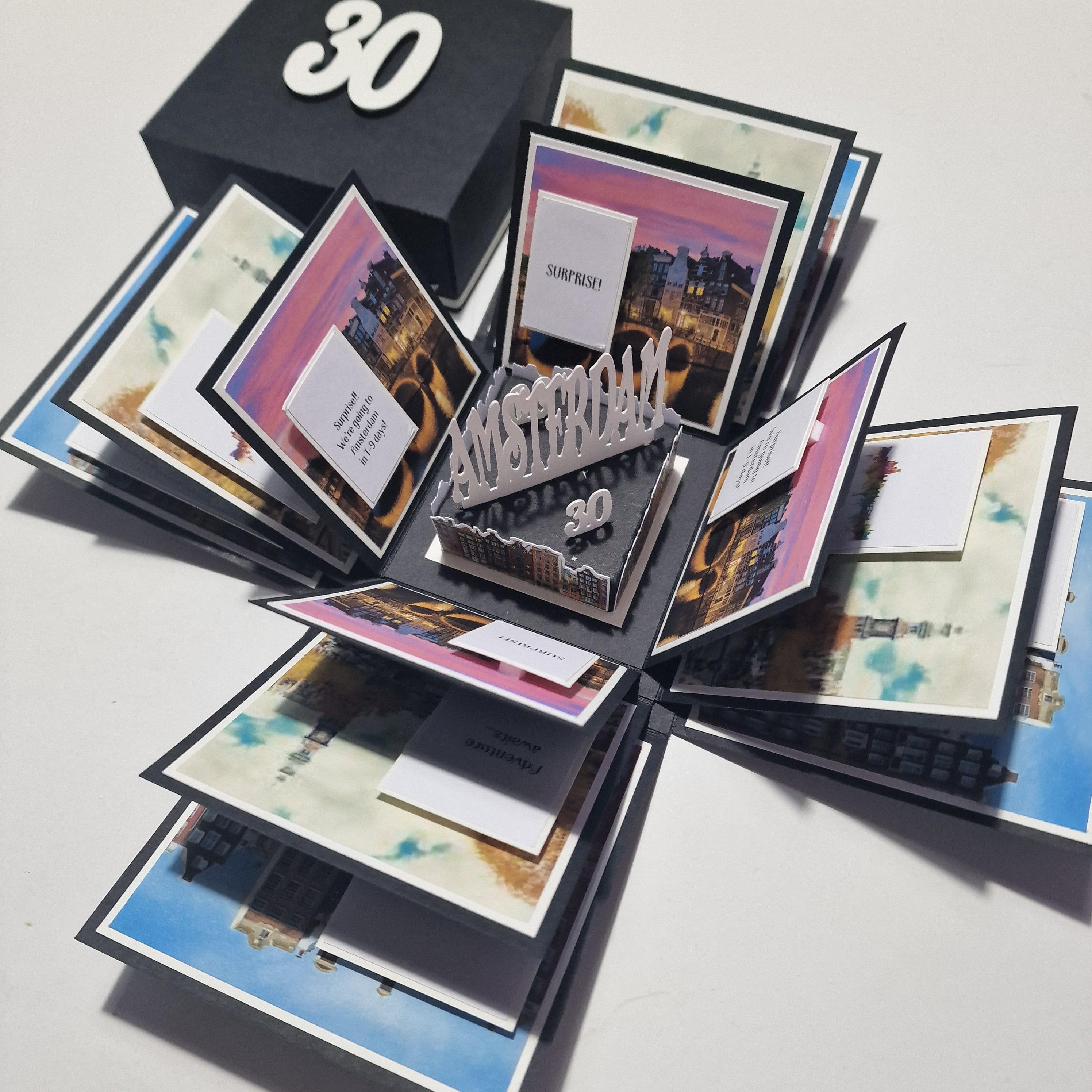 Exploding Occasions Box - Trip Reveal AMSTERDAM featuring a photo album, cityscape image, and themed paper panels, showcasing iconic Amsterdam canal houses, designed for a surprise trip announcement.