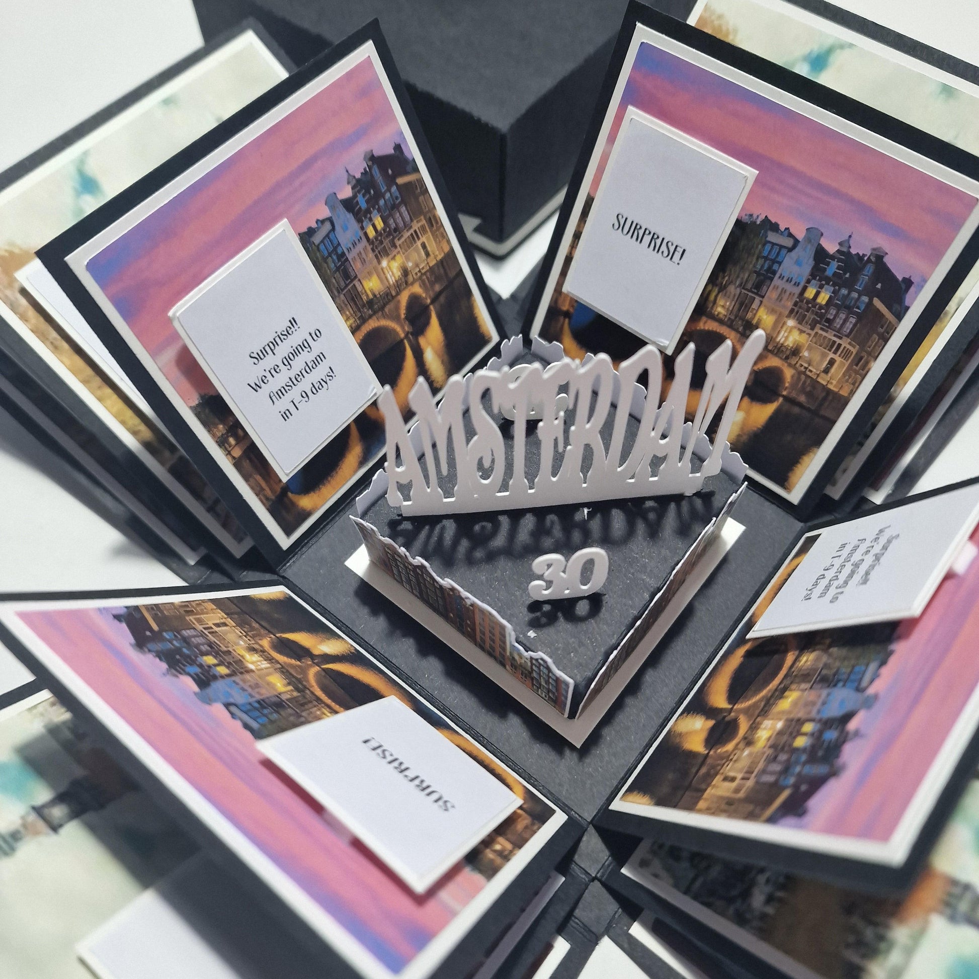 Exploding Occasions Box - Trip Reveal AMSTERDAM featuring intricate cityscape elements and personalized cards, designed as a surprise trip gift with Amsterdam-themed paper panels and freestanding canal houses.