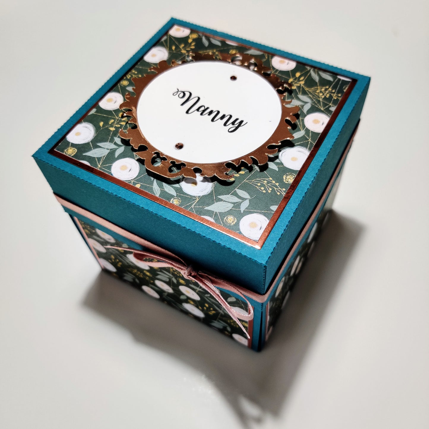 Bold Florals Birthday Celebration Pop-Open Box Card featuring a teal box with a gold ribbon, white circular cutouts, and intricate floral designs, showcasing a 3D paper flower arrangement inside.