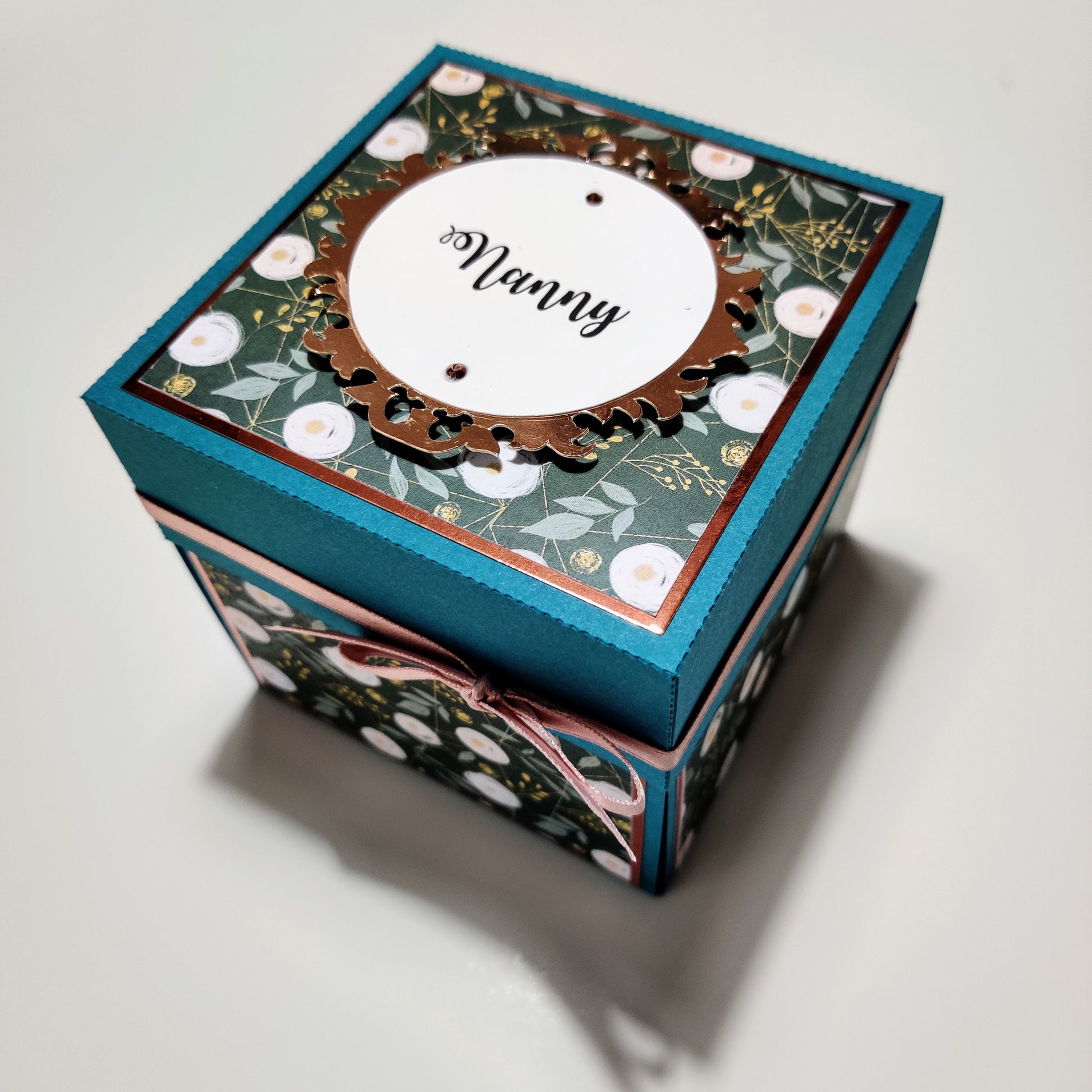 Bold Florals Birthday Celebration Pop-Open Box Card featuring a teal box with a gold ribbon, white circular cutouts, and intricate floral designs, showcasing a 3D paper flower arrangement inside.