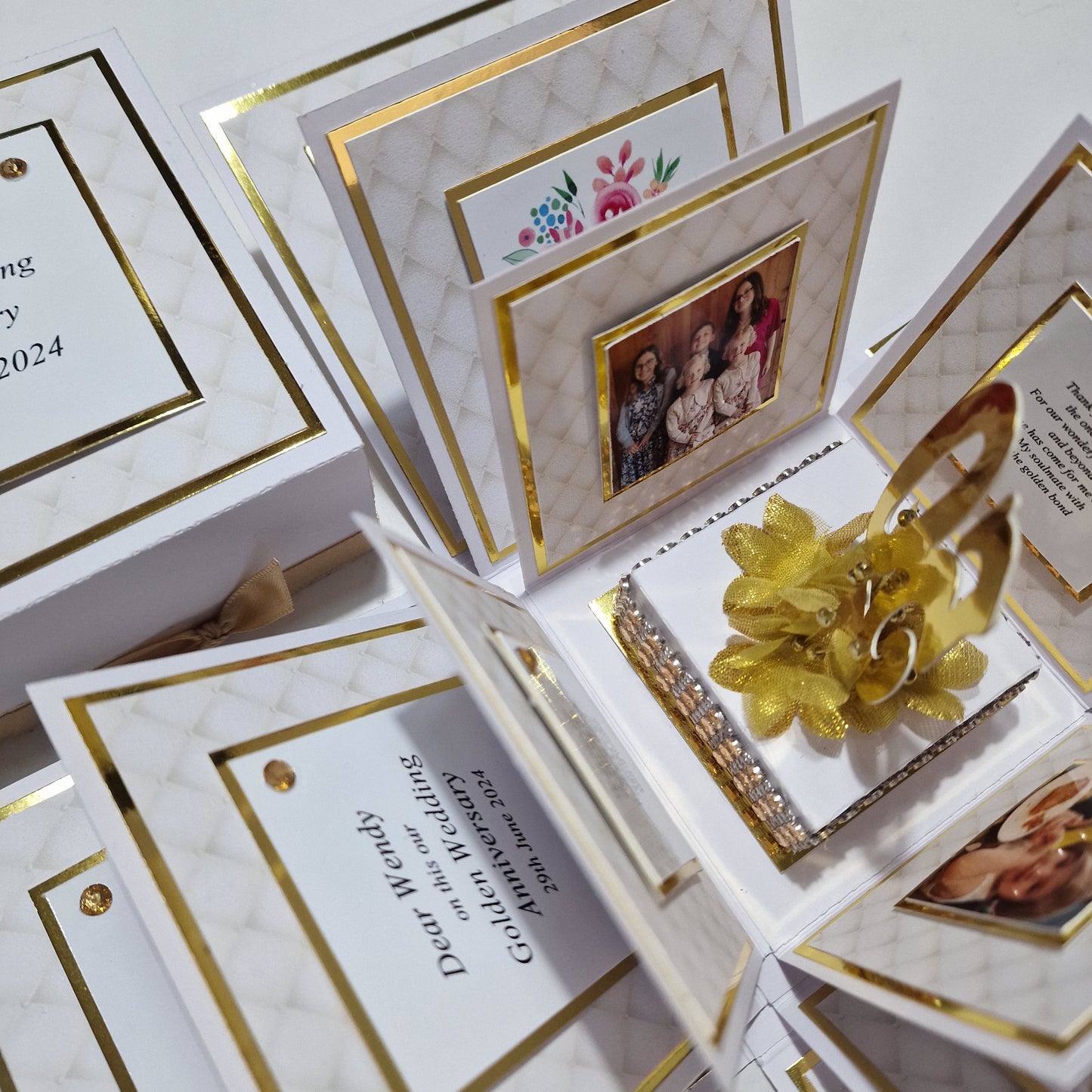 Golden Wedding Anniversary Exploding Box featuring a gold flower and ribbon on a white base, surrounded by cards with gold borders inside, ideal for personalized messages and photos.