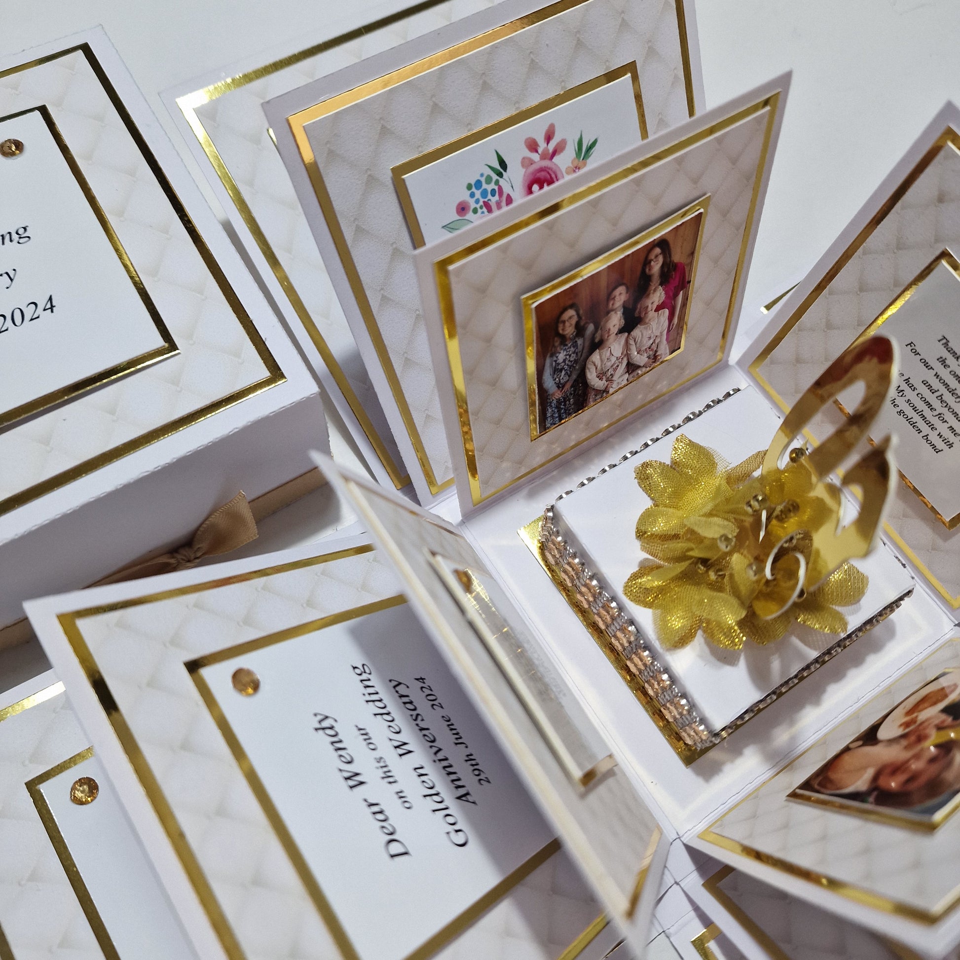 Golden Wedding Anniversary Exploding Box featuring a gold flower and ribbon on a white base, surrounded by cards with gold borders inside, ideal for personalized messages and photos.