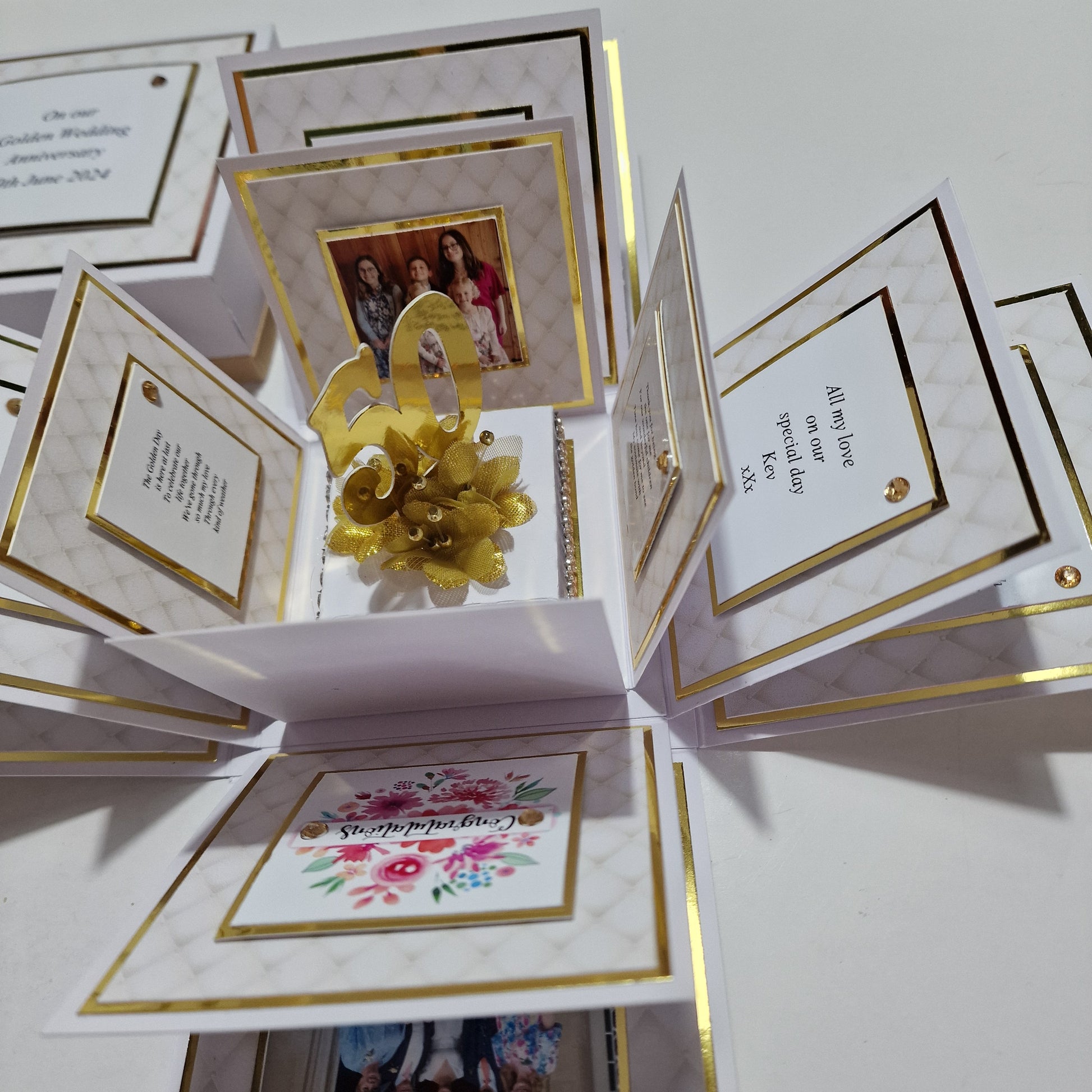 Golden Wedding Anniversary Exploding Box elegantly adorned with a gold bow and ribbon, showcasing floral cards, gold-accented plaques, and customizable photo areas, perfect for commemorating a 50th anniversary.