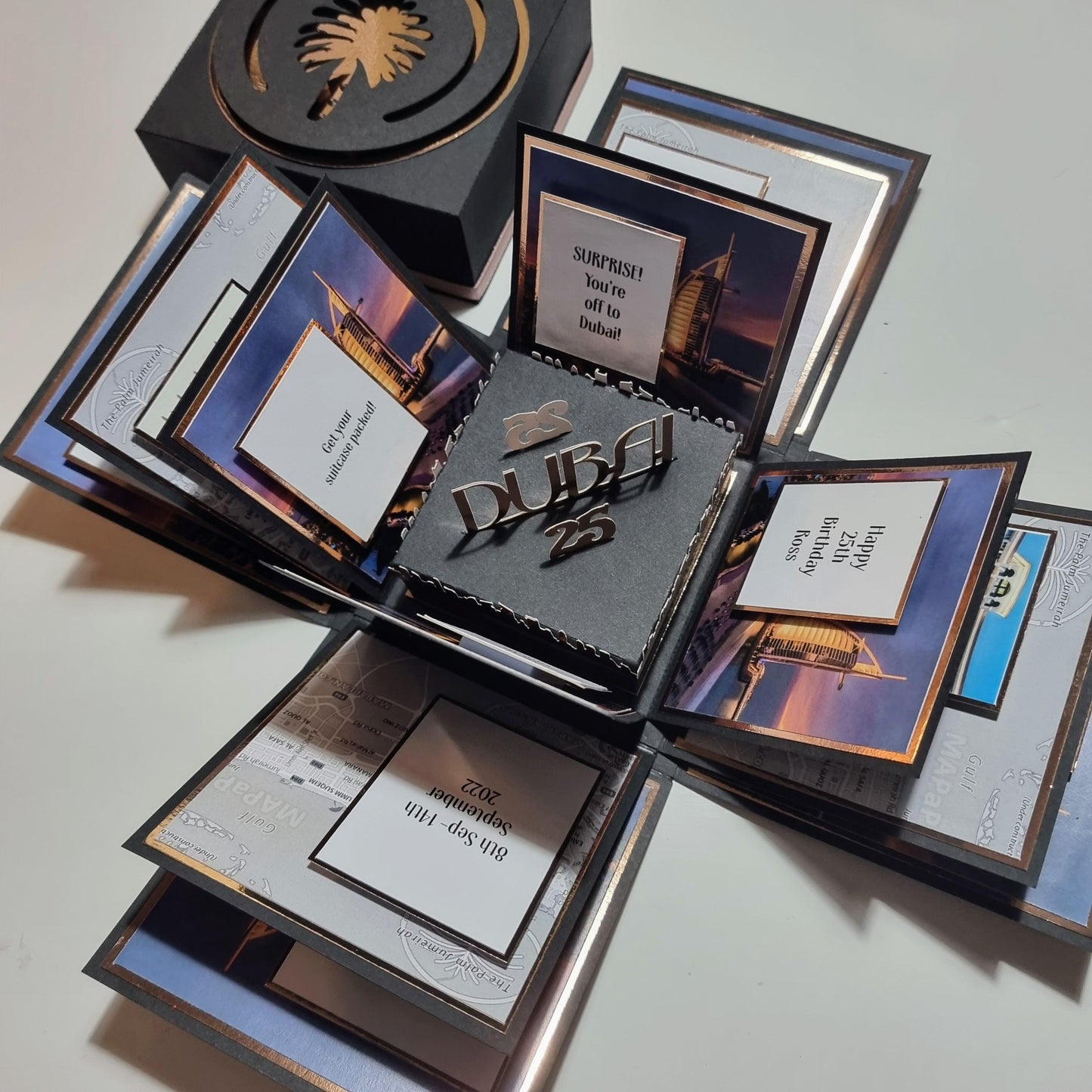 Exploding Occasions Box - Trip Reveal Dubai: A box with intricate panels featuring Dubai's iconic architecture and event details, designed for a surprise trip reveal. Includes space for personalized trip information.