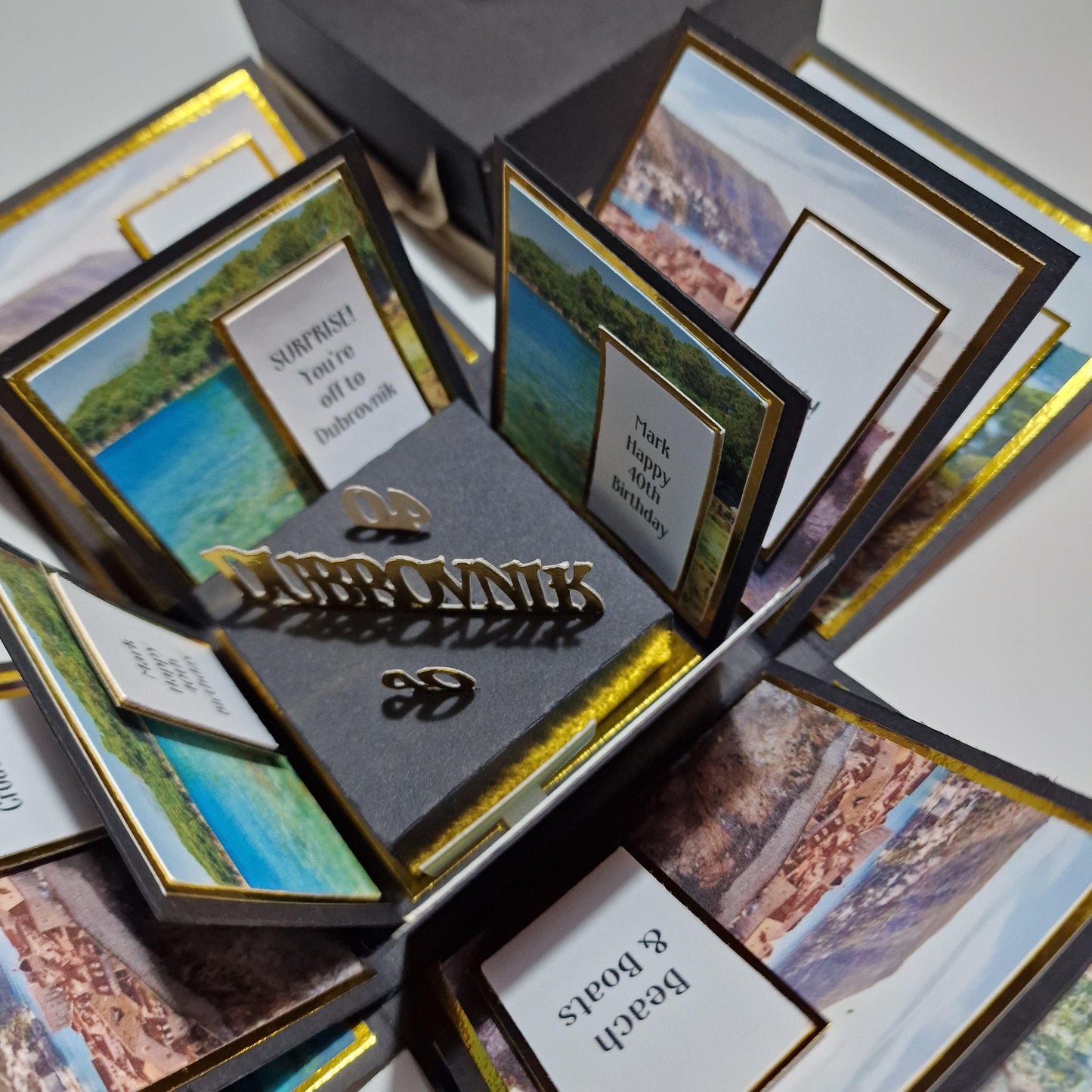 Exploding Trip Reveal Box - DUBROVNIK featuring a black box with multiple framed pictures and a white sign with black text, designed for special trip surprises with themed panels.