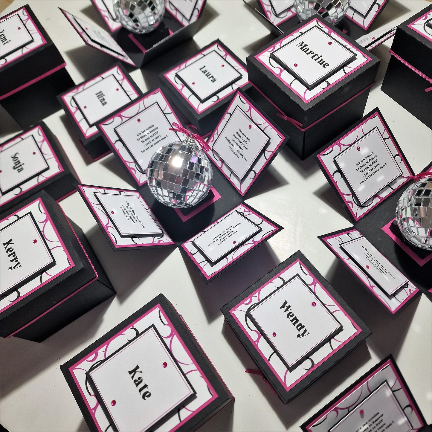 Box'd Disco Themed Invitation Boxes with custom design elements, featuring black boxes with white and pink labels, a mirror ball, and decorative cards, highlighting a unique wedding invitation concept.