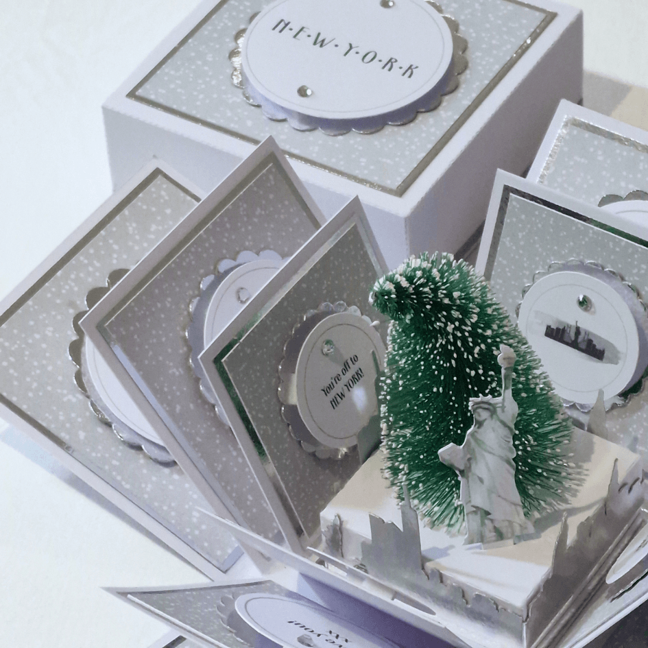 New York Christmas Trip Reveal Box featuring a miniature Statue of Liberty, Christmas tree, and New York skyline within a decorative box. Perfect for a personalized holiday surprise trip announcement.