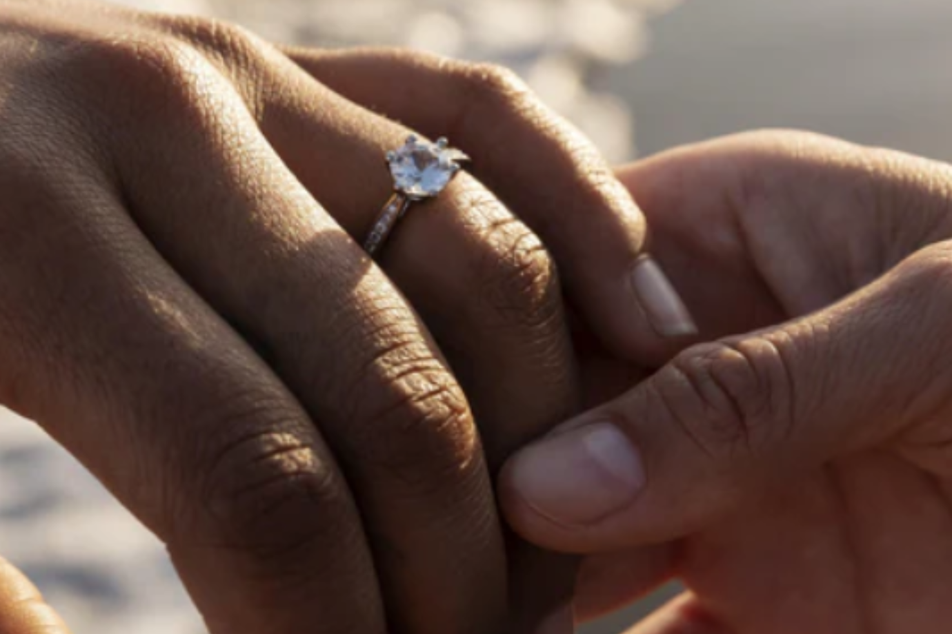 mans hand holding a woman's hand on which a large diamond engagement ring sits on her ring finger. Symbolising a new engagement.