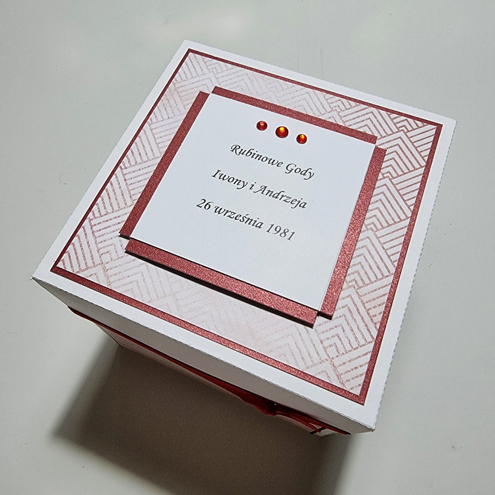 Ruby Wedding Anniversary Exploding Box: A white box with red ribbon and card, featuring intricate black text, perfect for celebrating a 50th wedding anniversary with personalized messages and photos.