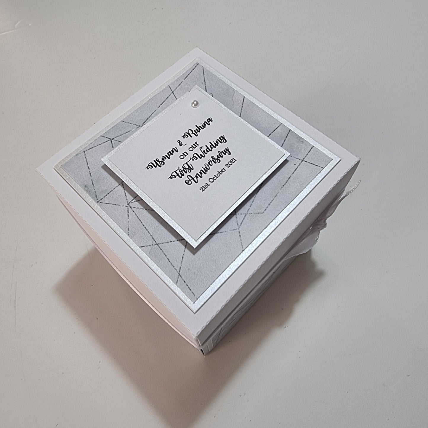 First Wedding Anniversary Exploding Box featuring a white box with a card on top, showcasing a square design. Perfect for adding personalized messages and photos, ideal for a memorable celebration.