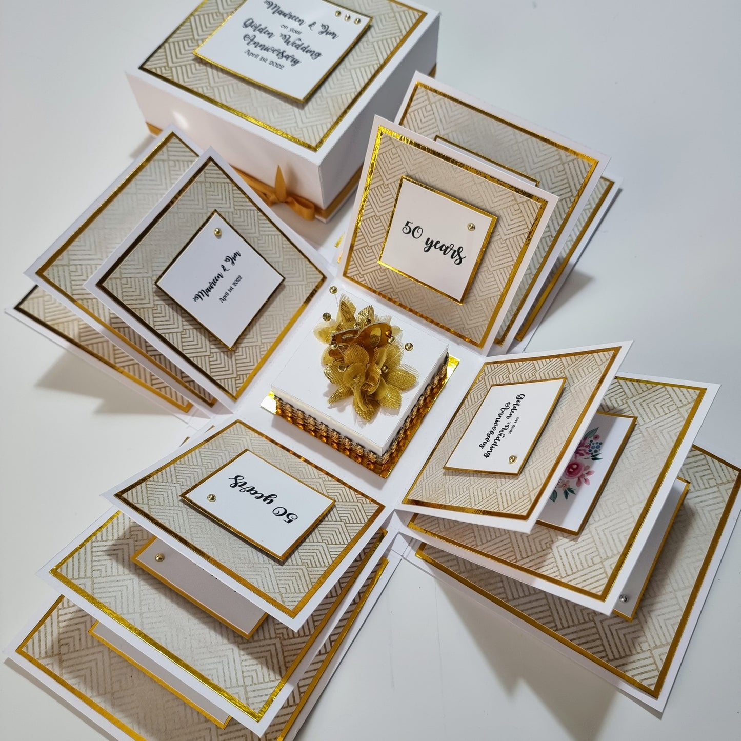 Golden Wedding Anniversary Exploding Box with a gold bow, white box, and golden accents. Features elegant design, customizable panels, and commemorative messages for a 50th anniversary keepsake.