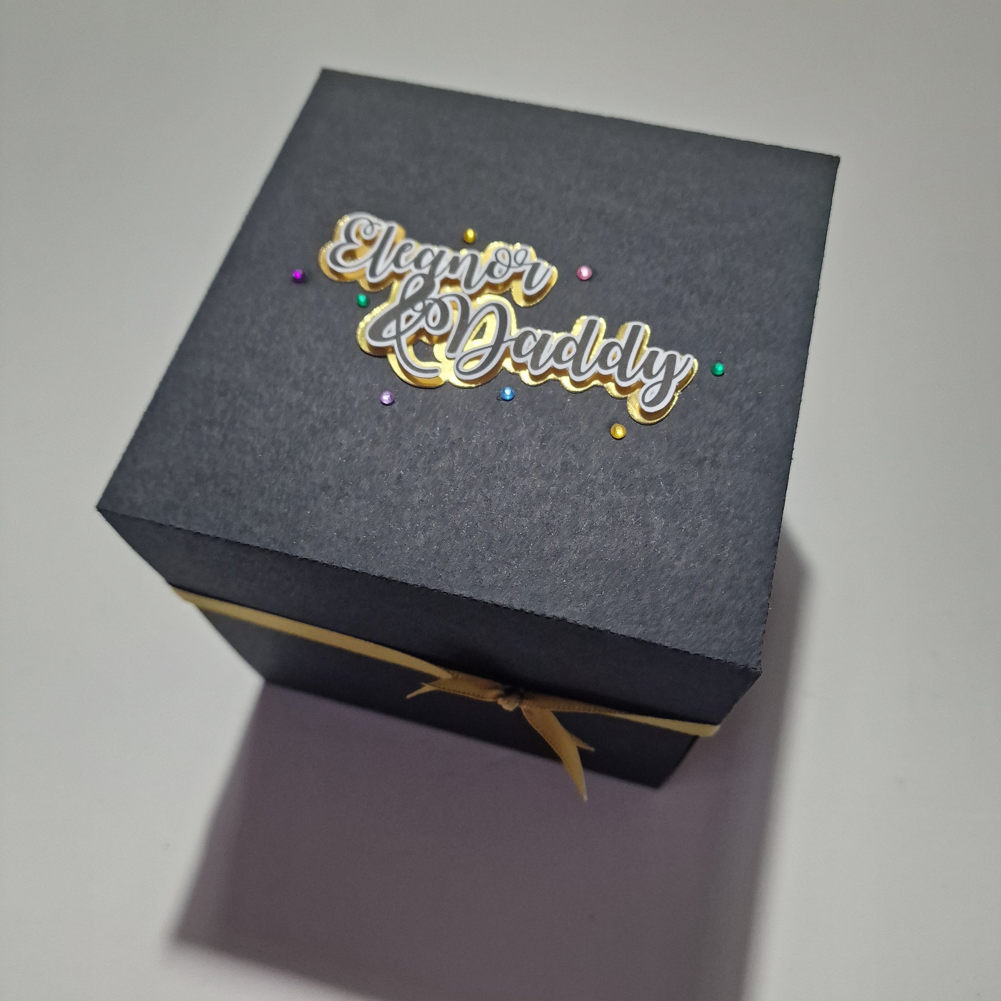 black box with gold ribbon, Two names and different coloured gem on the top