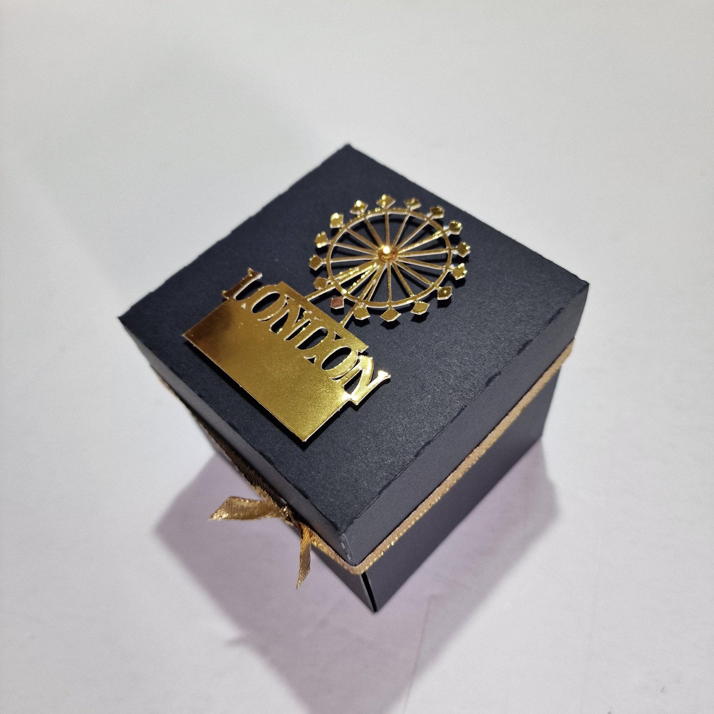 Exploding Occasions Box - Trip Reveal LONDON, featuring a black box with a gold logo and text, designed as an exciting surprise gift for a London-themed trip reveal.