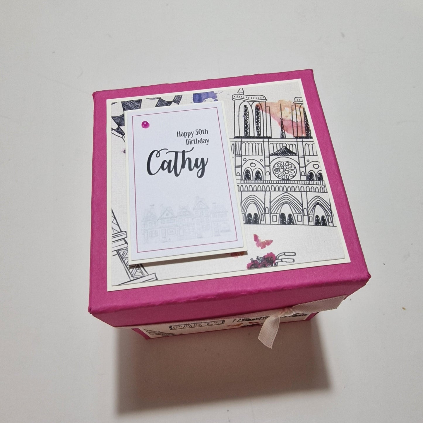 Exploding Occasions Box - Trip Reveal PARIS: A pink box with a white label, featuring a freestanding Eiffel Tower and Paris-themed paper panels, ideal for surprise trip announcements.