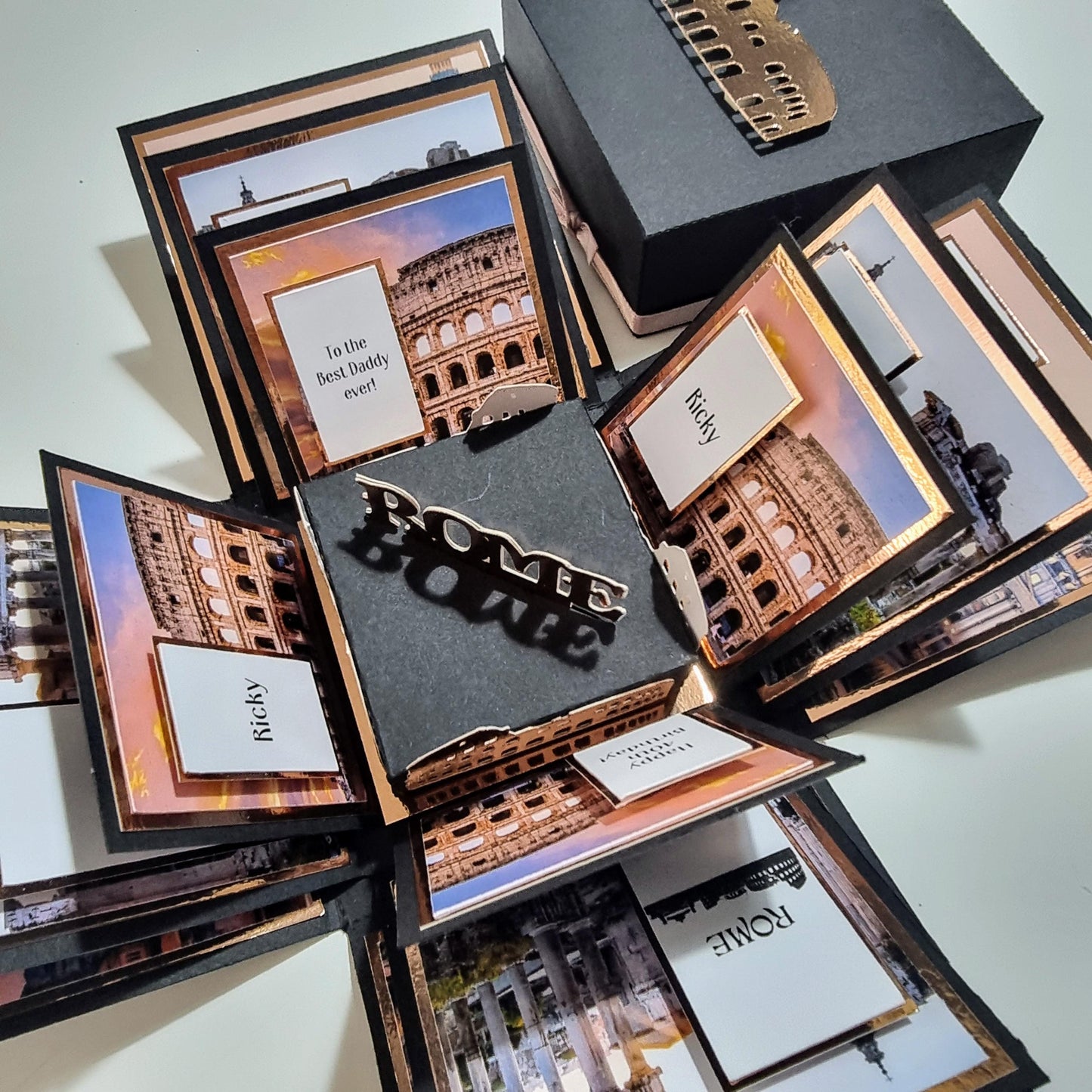 Exploding Occasions Box - Trip Reveal ROME featuring a photo of Rome's Colosseum, black and gold thematic design, and personalized trip details on white and black panels.