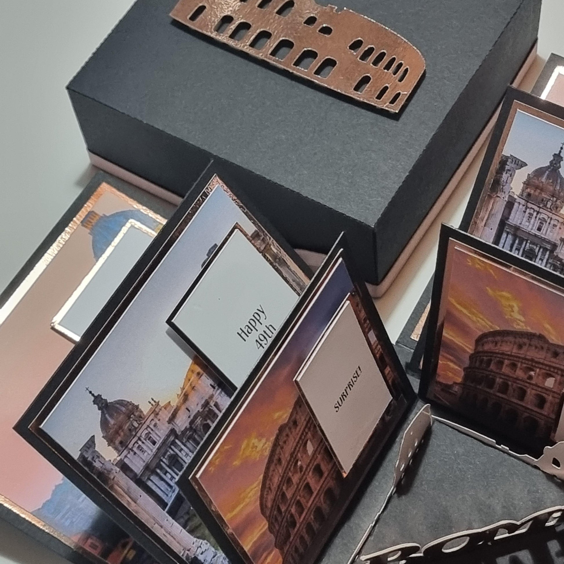 Exploding Occasions Box - Trip Reveal ROME featuring intricate paper cutouts of the Colosseum, cards, and a box designed to celebrate a surprise trip with personalized details.