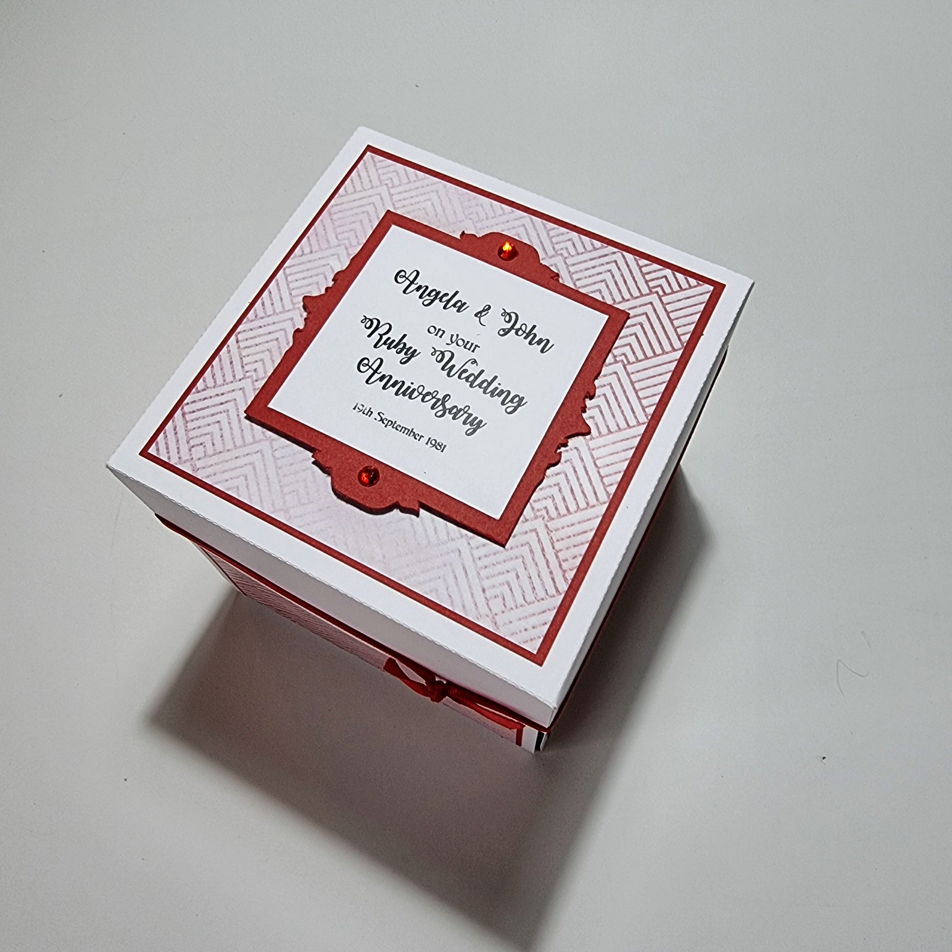 Ruby Wedding Anniversary Exploding Box featuring a white box adorned with a red and white ribbon. The keepsake box symbolizes love, with customizable panels for names, dates, and personal messages.