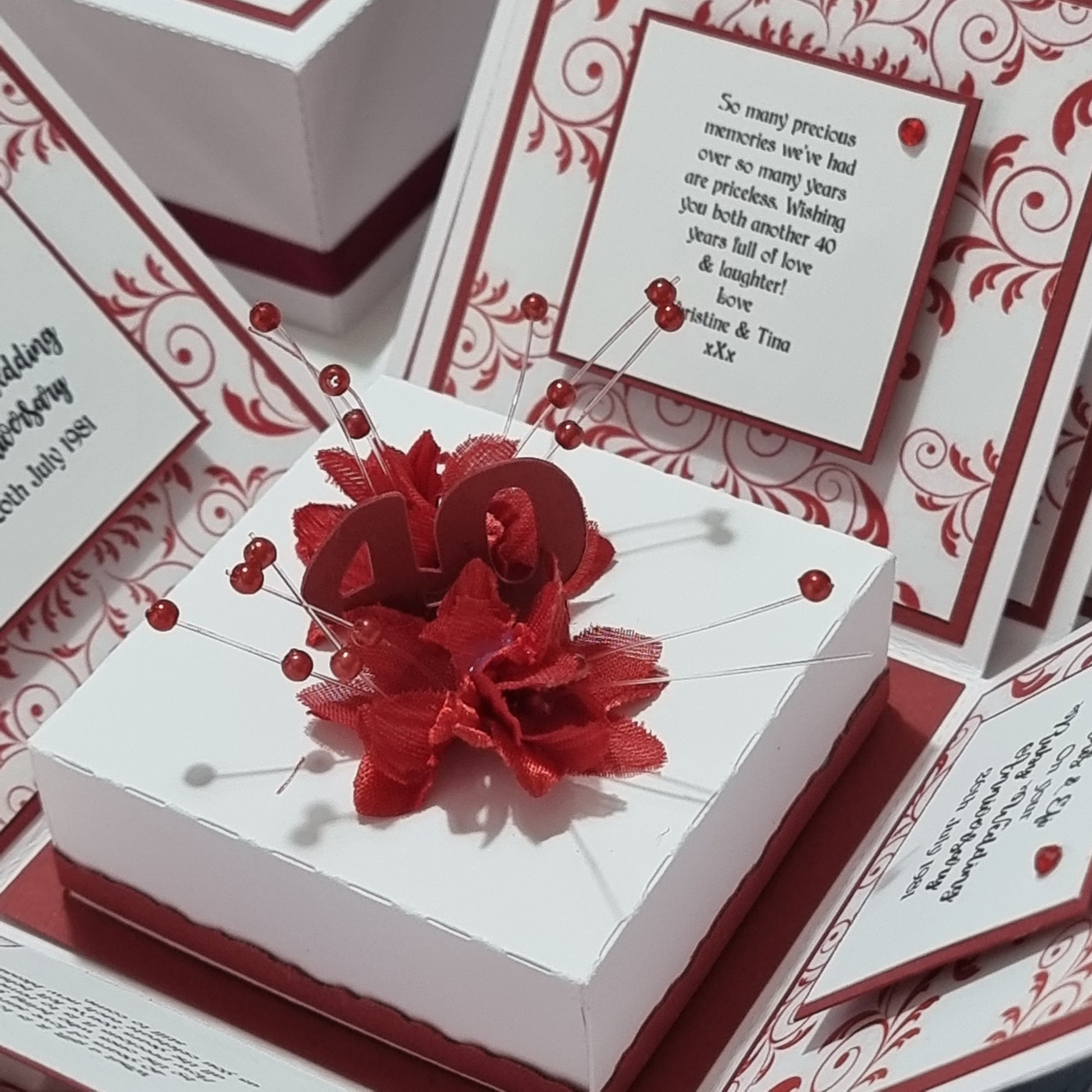 Ruby Wedding Anniversary Exploding Box featuring a white exterior adorned with red flowers and ribbon, offering a personalized keepsake with space for names, date, messages, and photos inside.