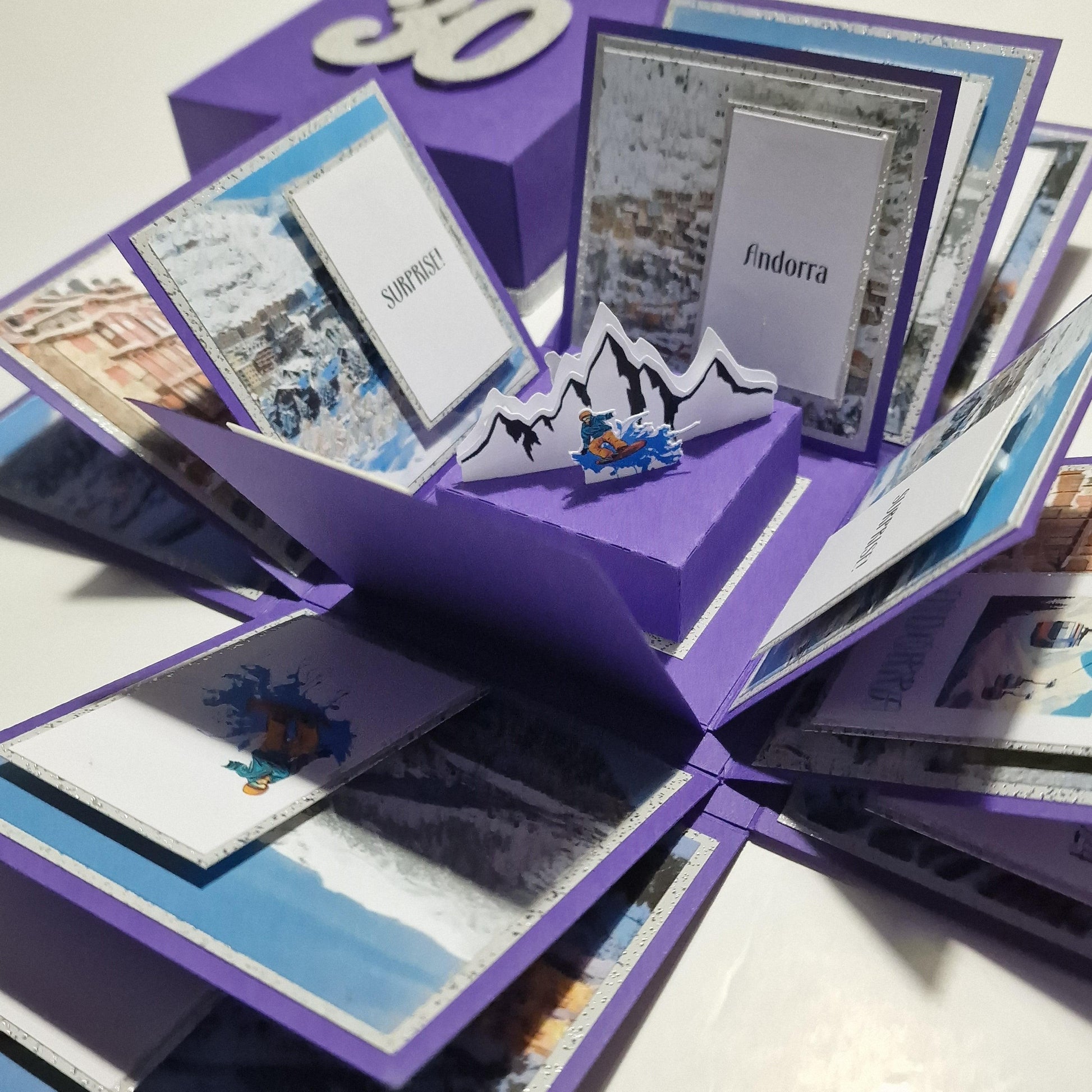 Exploding Occasions Box - Trip Reveal - Custom Occasion, featuring a purple box with mountain and snowboarder images, designed to unveil surprise trip details with personalized panels and messages.