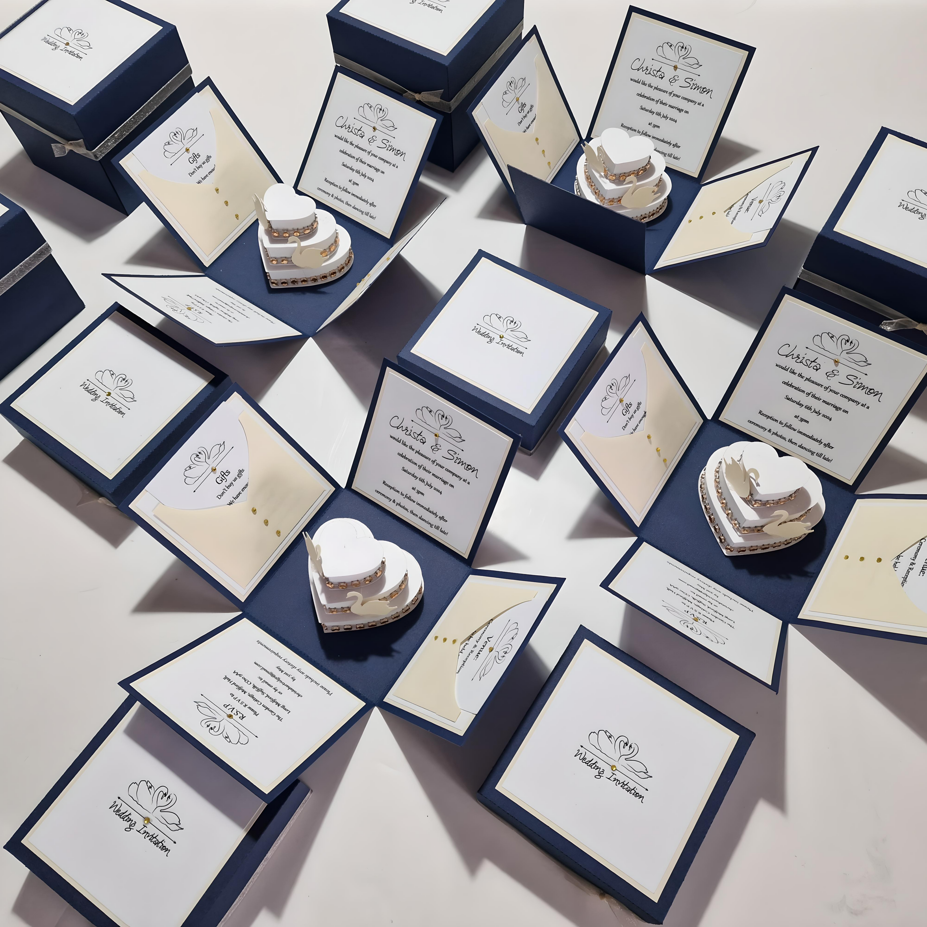 Swans Pocket Exploding Wedding Invitation Boxes feature a heart-shaped cake with swans, gold ribbons, and a three-tier design as the centerpiece, surrounded by elegant cards and swan motifs.