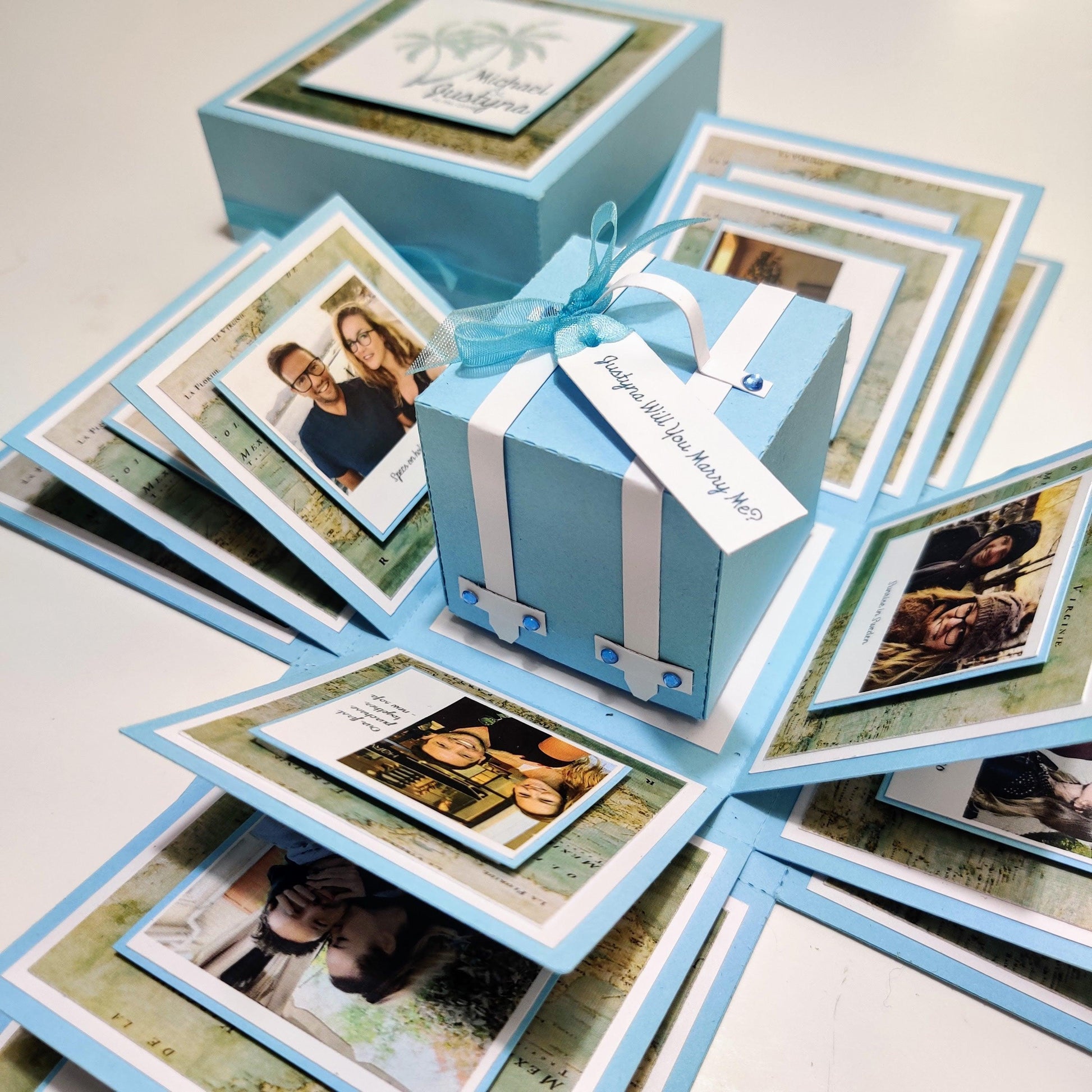 Travel Themed Proposal Box featuring a blue box with a white ribbon, designed for unique engagement proposals. Includes personalized photo panels and messages, enhancing the memorable ring presentation.