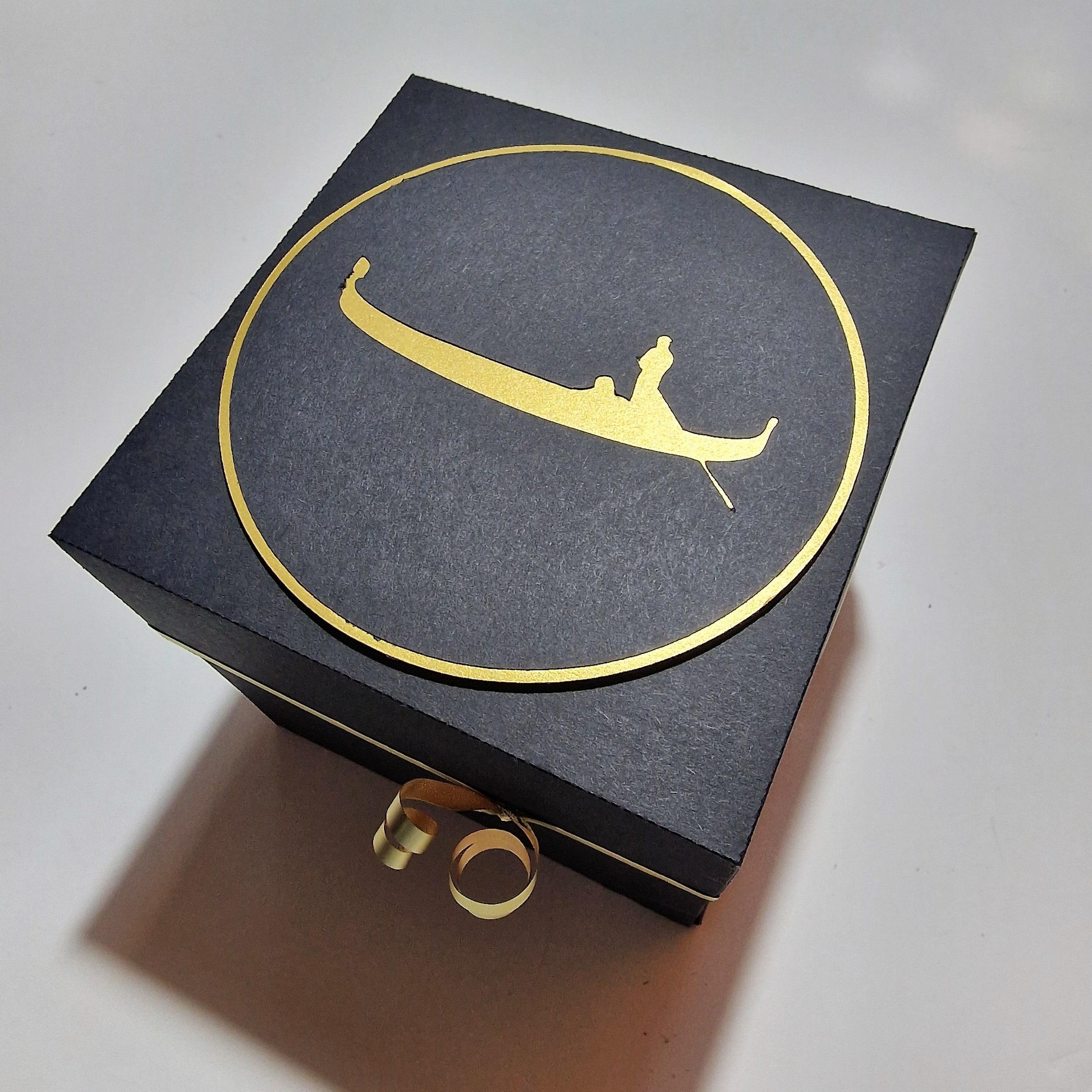 Exploding Occasions Box - Trip Reveal VENICE, featuring a black box with a gold logo and ribbon, designed for a Venice-themed surprise with intricate paper and architectural panels inside.