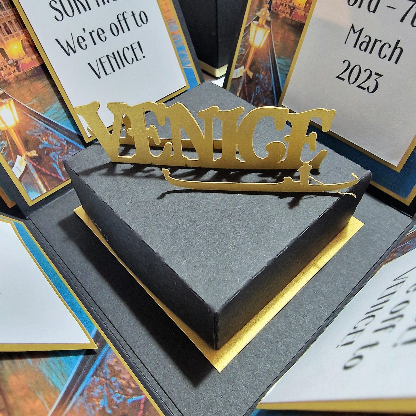 Exploding Occasions Box - Trip Reveal VENICE, a black square box with gold lettering, designed for surprise trip announcements, featuring Venice-themed panels and a freestanding gondola centerpiece.