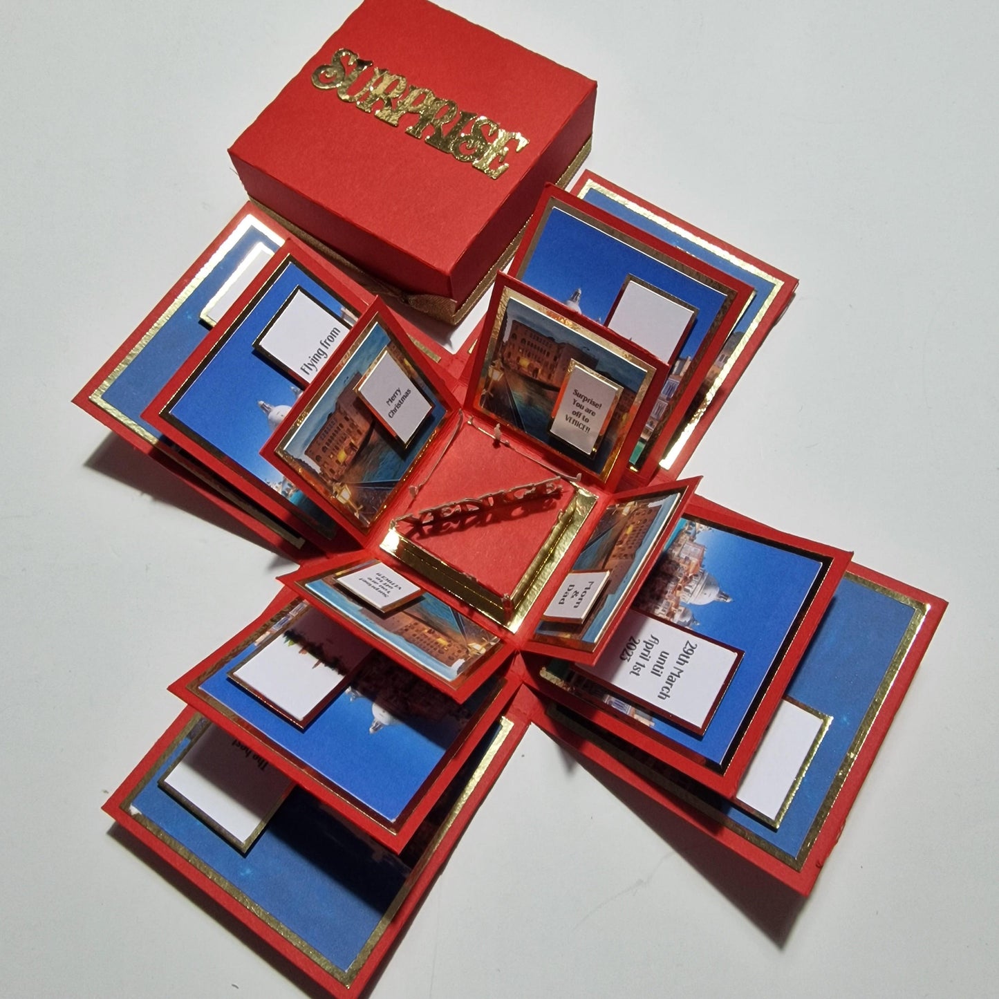 Exploding Occasions Box - Trip Reveal VENICE features a red box with gold lettering and intricate designs, showcasing Venice-themed elements like a gondola and architectural panels for a surprise trip reveal.