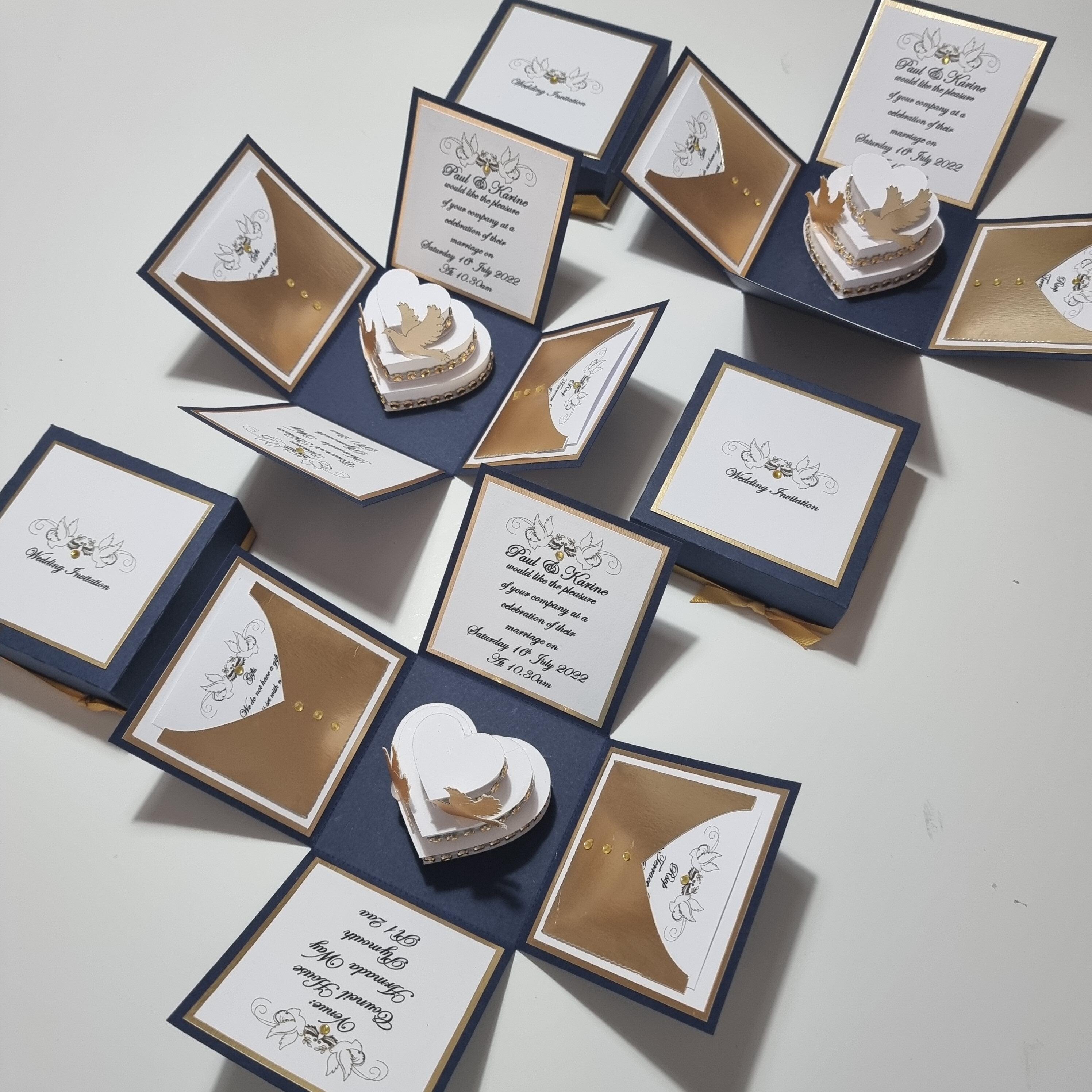 Navy Blue & Gold Exploding Wedding Invitation Boxes featuring intricate card designs, heart-shaped cake with doves, and detailed invitation elements like RSVP and menu cards. Luxurious and customizable wedding stationery.